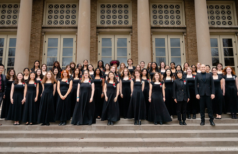 Large choir posed on steps outside a columned building.