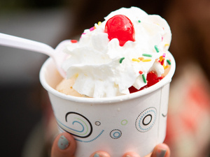 A cup of ice cream with whipped cream, sprinkles and a cherry on top.