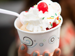 A cup of ice cream with whipped cream, sprinkles and a cherry on top.