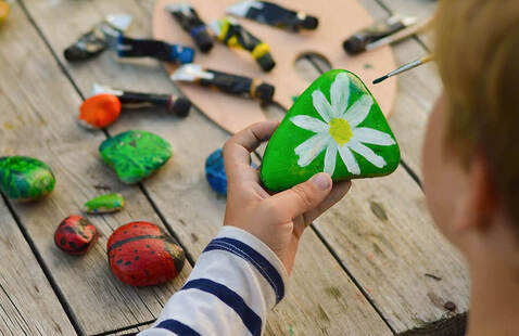 A child's hand holds a painted rock, with more painted rocks in the background