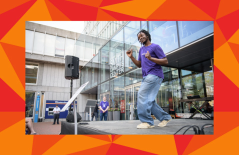 A male contemporary dancer wearing a purple shirt, jeans, and white sneakers dances on a stage outside the Smith Campus Center.