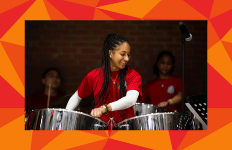 Members of the Harvard College Steelpan Ensemble playing steel drums while wearing red t-shirts.