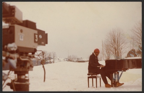 Randy Weston plays a grand piano outside on a snowy field.