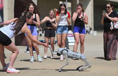Students reaching out to a robotic dog at the fine arts center
