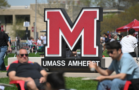 People sitting outside in front of the UMass Amherst Big M sign 