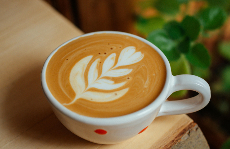 Cup of coffee with leaf-shaped latte art on a wooden surface.