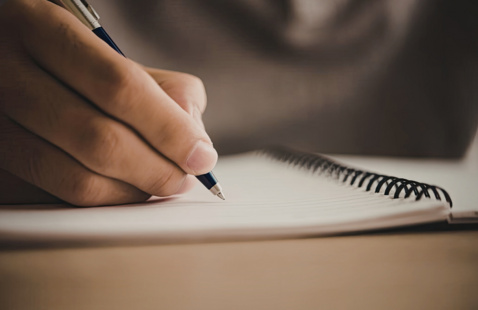 Close up of someone writing in a notebook with a pen