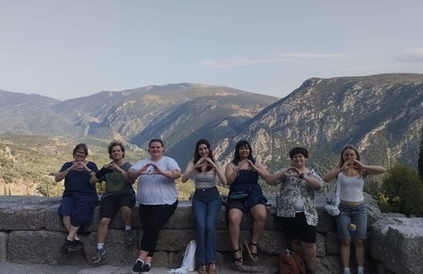a group of students throw their 'o' with a hilly, green landscape in the background and a blue sky