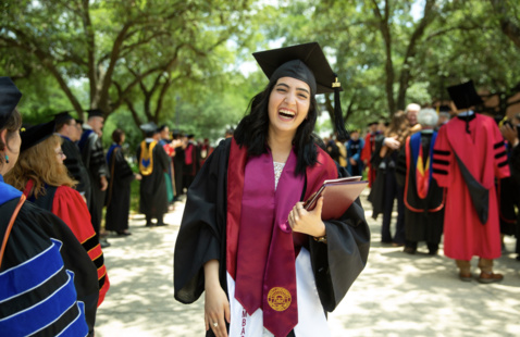 Trinity graduate wearing a commencement hoot and cap walking past other graduates
