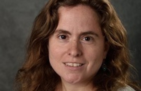 Woman smiling at camera wearing dark shirt and light sweater.