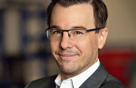 Photo of Steven Skerlos, a light-skinned man with short brown hair, wearing glasses, a white collared shirt, and a gray suit.