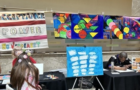 A colorful array of artwork is on display. It is being viewed by a patron in a wheelchair.
