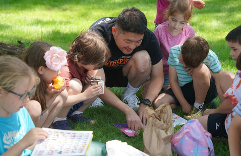 Campers eating lunch and looking at the book their Camp Counselor is reading to them outside.