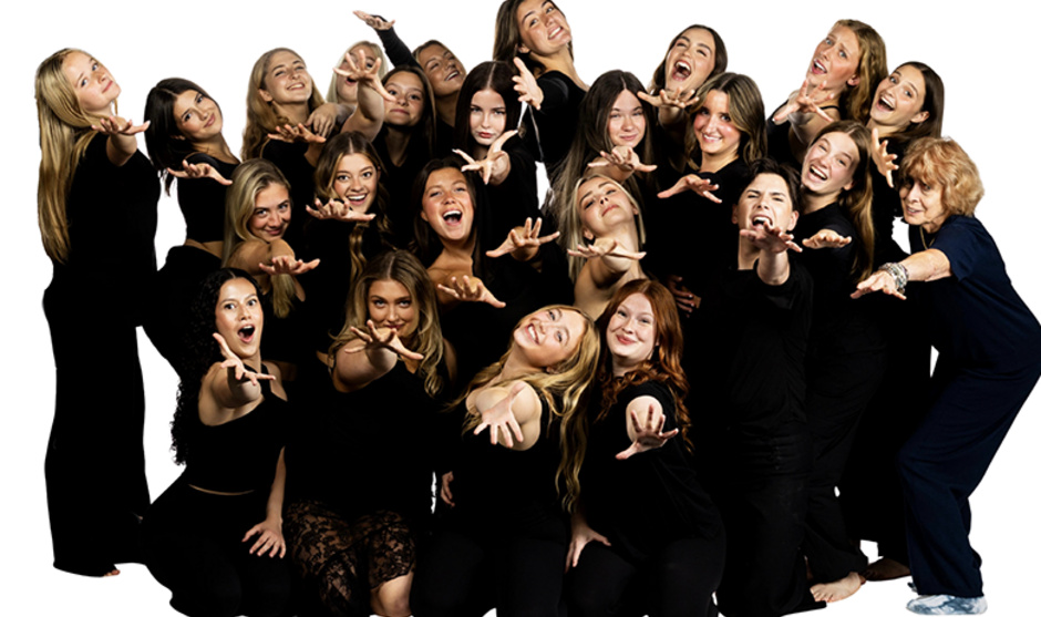 A group of 21 Dance Theatre members in black dancewear pose with arms outstretched