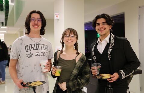 Three Students smiling holding plates of pancakes and sausage with orange juice