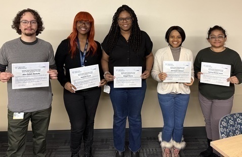 lineup of 5 students holding up pieces of paper.