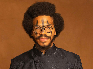 KAMAUU wears a black coat and faces the camera