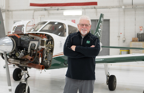 Dan Kasowski smiling, arms crossed, in front of airplane in hangar for maintenance