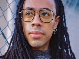 Profile picture of Alan Pelaez Lopez with a chained fence in the background. Alan is wearing a black leather jacket and gray sweater.