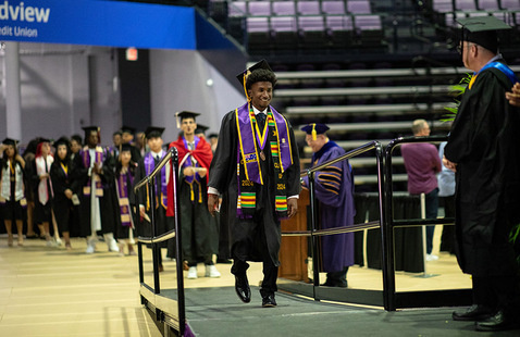 Student in regalia walking up a ramp towards faculty members.