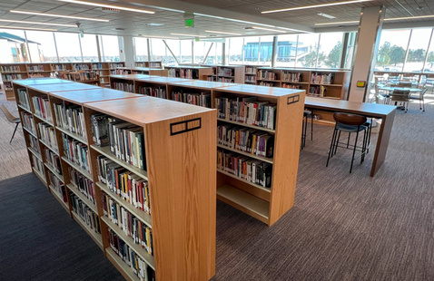 Photo of bookshelves full of library materials and study tables in the Learning Commons at the Greeley campus
