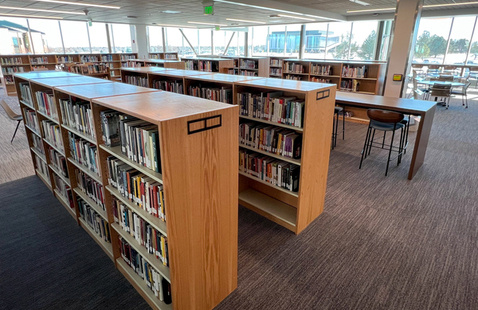 Photo of bookshelves full of library materials and study tables in the Learning Commons at the Greeley campus