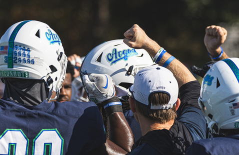 Three UWF football players in football helmets displaying Argos on the side with a coach wearing hat displaying Argos on the back.