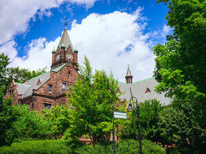 Mary Lyon Hall with beautiful green trees and a bright blue sky and white clouds. 