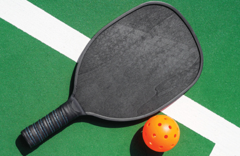 A paddle and wiffle ball sitting at the edge of a court.