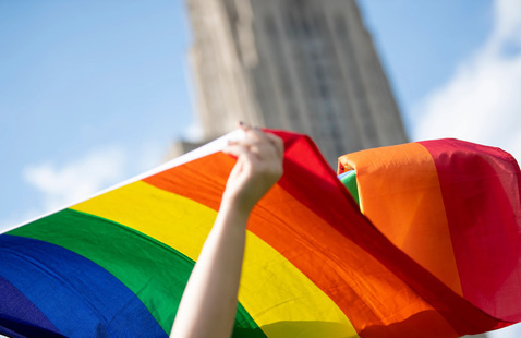 Person waves pride flag outside Cathedral of Learning