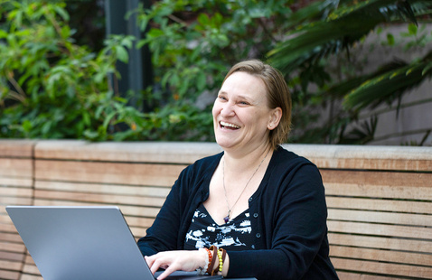 Woman sitting on a bench with her laptop and smiling.