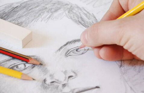 A hand shown holding a pencil while drawing a face