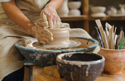 Person sitting at potter wheel forming clay