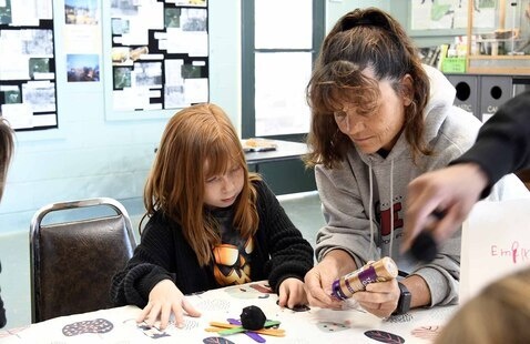 An adult and a child complete a craft together at a table inside the Paynetown Activity Center.