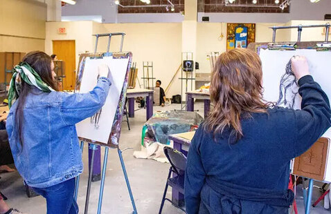 Two people in art room drawing on canvas with easel