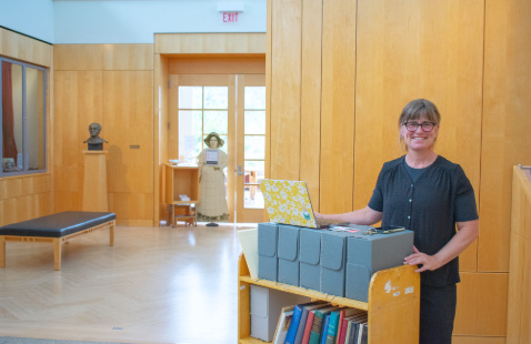 woman standing in front of the library's fifth floor foyer with a book cart full of books and boxes
