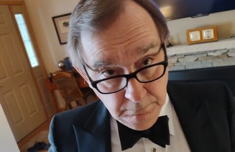 Man in tuxedo, looking over glasses, taking selfie