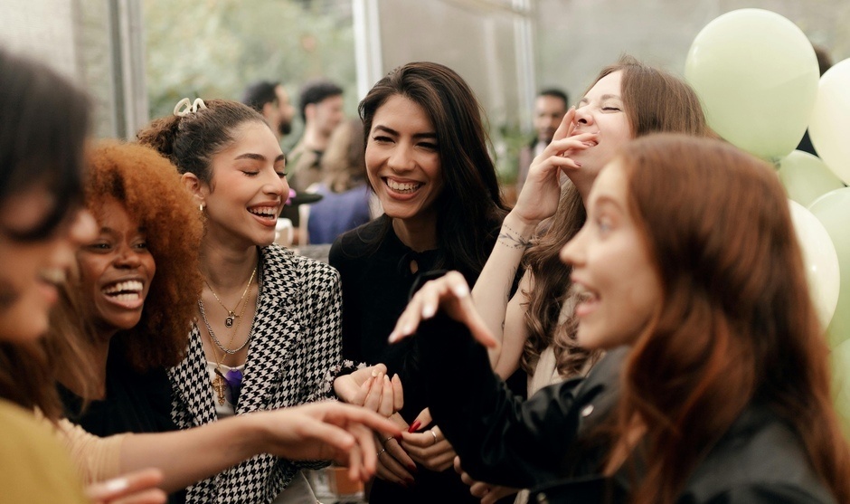A joyful gathering of young adults laughing and socializing at a party inside a bright venue