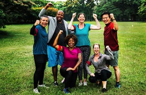 A group of people wearing athletic gear. They are in a grassy park and are holding their arms up in triumph and achievement.