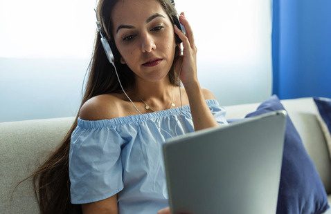 A woman wearing headphones looks at something on her tablet computer.