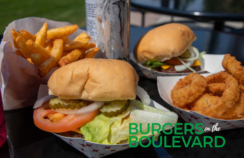Two freshly grilled cheeseburgers with all the fixings, with a side of onion rings and a side of French fries.
