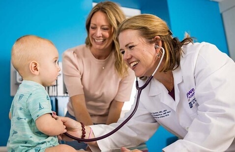 Doctor uses stethoscope to check an infant with smiling mom watching on.