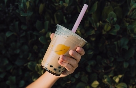 image of an arm holding a boba milk tea with bushes in the background.