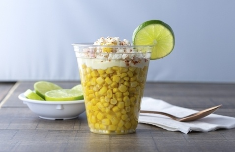 image of a cup of corn with cheese and mayonnaise on top, a lime is attached to the rim of the  cup.