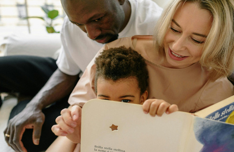 Interracial family enjoying quality time reading a book indoors together.
