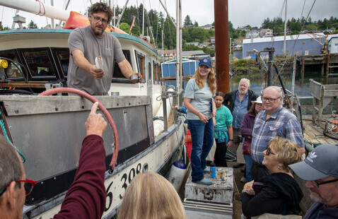 A fisherman hands out canned fish to a group of people on a dock.