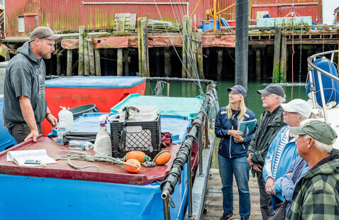 A fishermen speaks to a group of people on a dock.