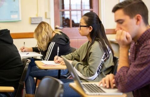 Three students taking notes while sitting in a classroom.