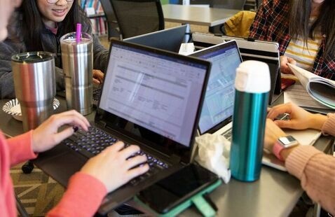 A group of four people sitting together at a table and typing on laptops.