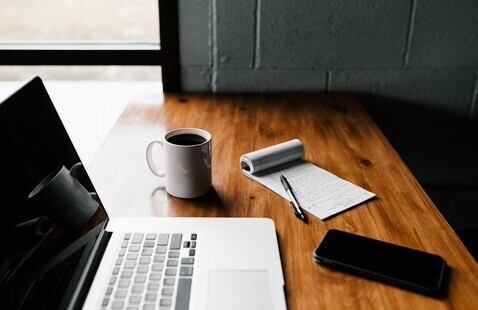 laptop, mug, paper pad and phone on desk